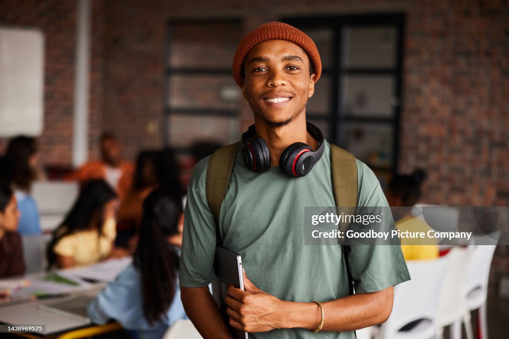 Smiling young male college student wearing headphones standing in a classroom