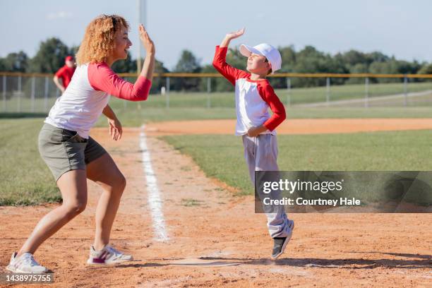 little boy jumps to give coach a high five after running to home base during baseball game - baseball team stock pictures, royalty-free photos & images