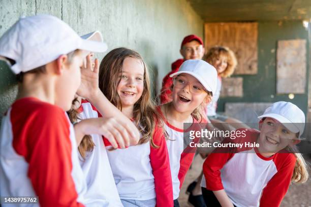 excited group of children laugh while sitting in dugout during baseball game - ungdomsliga för baseboll och softboll bildbanksfoton och bilder