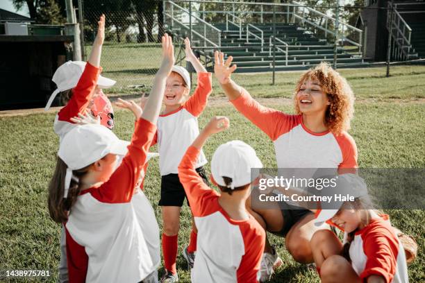 young woman is coaching little league team and huddling with them during game - baseball huddle stock pictures, royalty-free photos & images