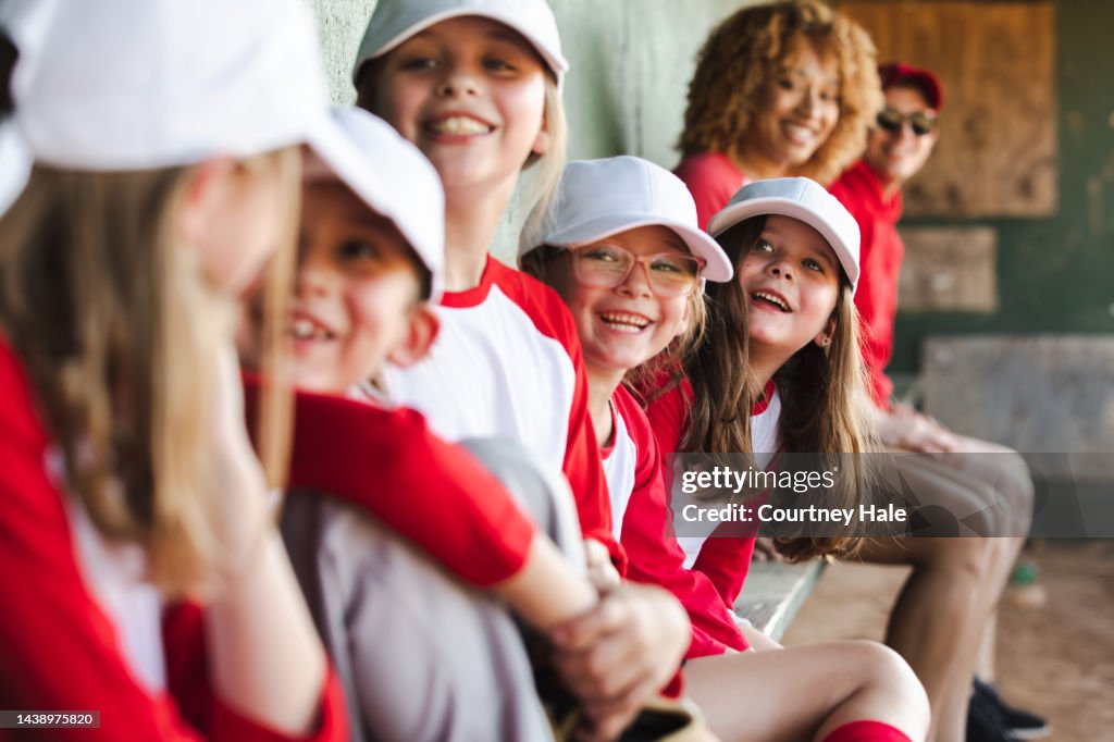 Little league team has fun together while sitting in dugout during baseball game