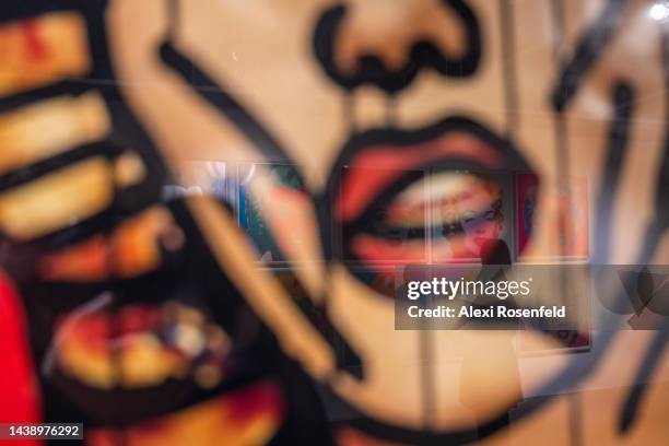 Woman looking at Andy Warhol's 'Marilyn Monroe' ten completed screen prints is reflected off Keith Haring's 'Untitled' during a media preview at...