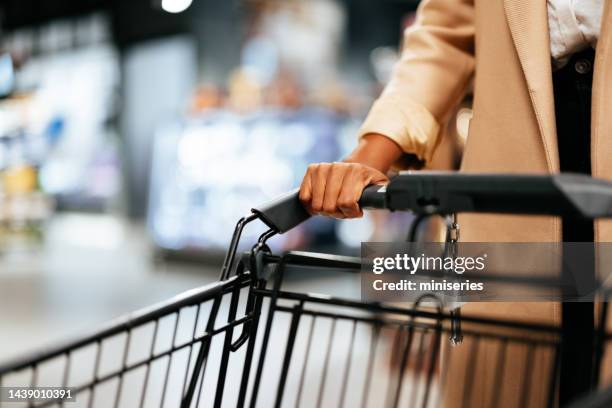 donna anonima in un cappotto che spinge un carrello della spesa - wagon foto e immagini stock