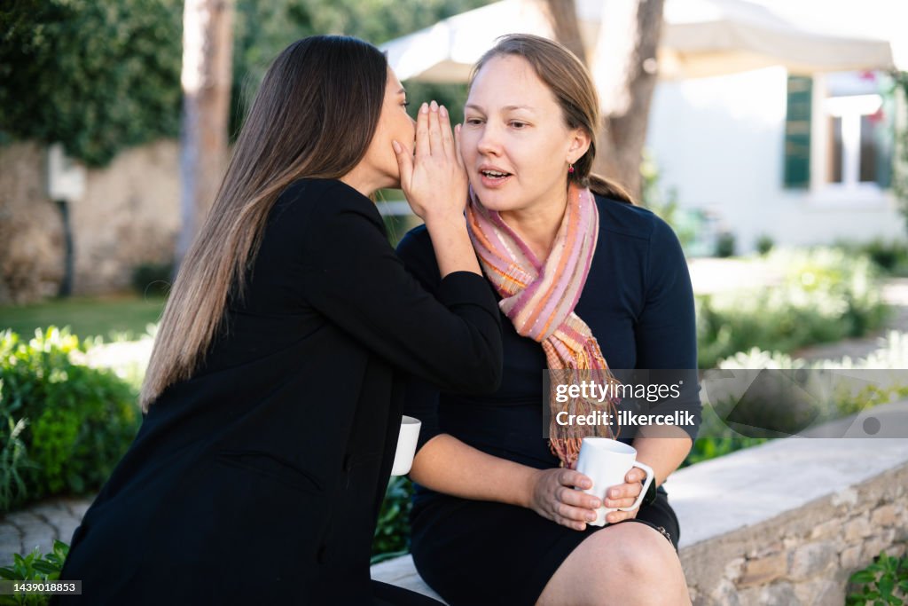 Frauen, die ihrer Freundin ins Ohr flüstern und sie überraschen