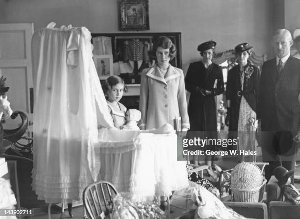 Princesses Elizabeth and Margaret next to the cot in which Margaret used to sleep, at an exhibition of royal treasures at 145 Piccadilly, London,...