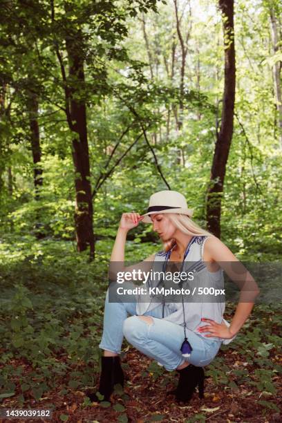 blonde girl wearing jeans,top,heels and summer hat in a green park kmphoto - kmphoto stock pictures, royalty-free photos & images