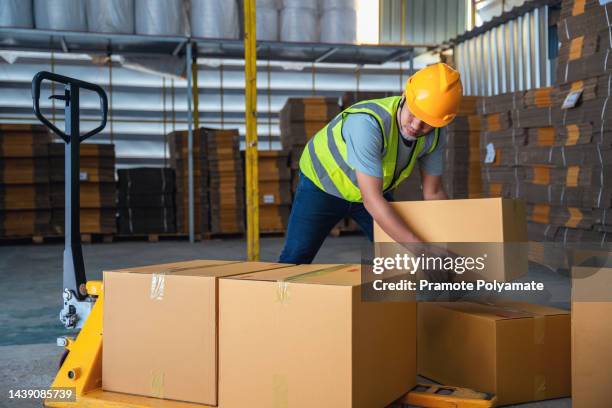 warehouse worker lifting cardboard boxes on a pallet truck in a large industrial warehouse. - box lifting technique stock-fotos und bilder