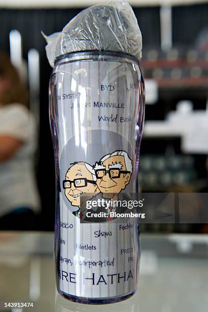 An insulated mug bearing an image of Warren Buffett, chairman of Berkshire Hathaway Inc., left, and Charlie Munger, vice chairman of Berkshire, sits...