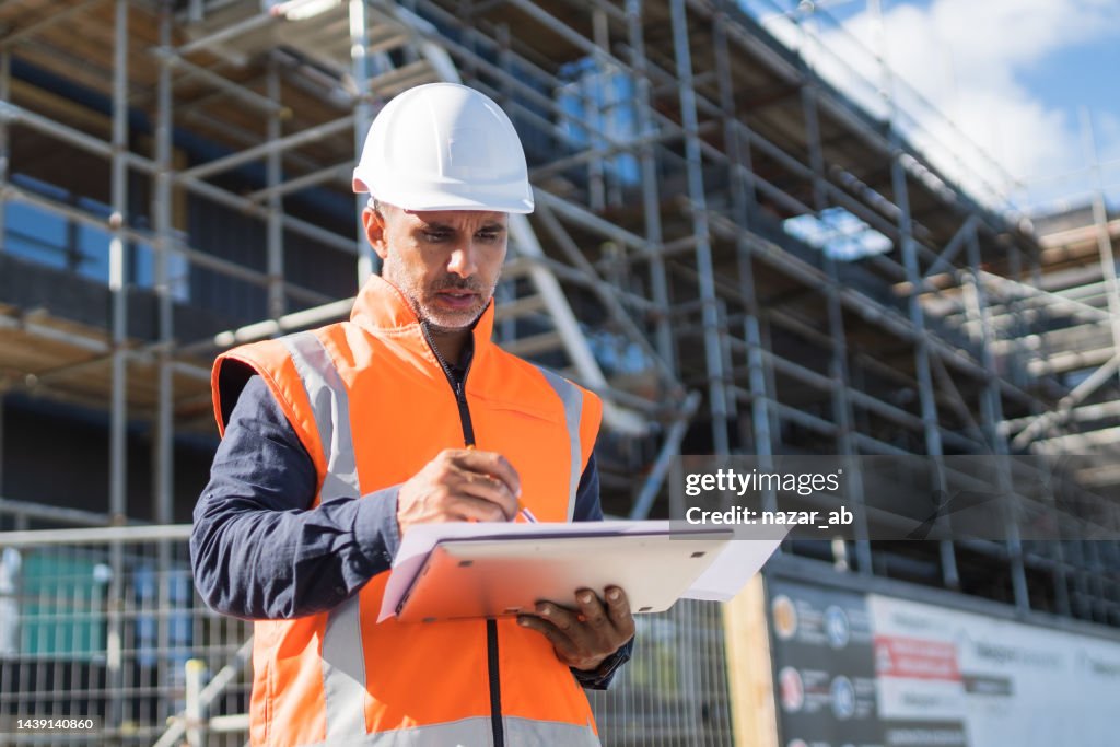 Engineer in protective clothing on worksite with digital blueprints.