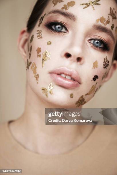 a young woman in a beige suit stands on a beige background with gold decorative stickers on the face with copy space. the beauty concept, halloween, party, makeup, meadow, summer or insects lover. - girl power stickers stock pictures, royalty-free photos & images