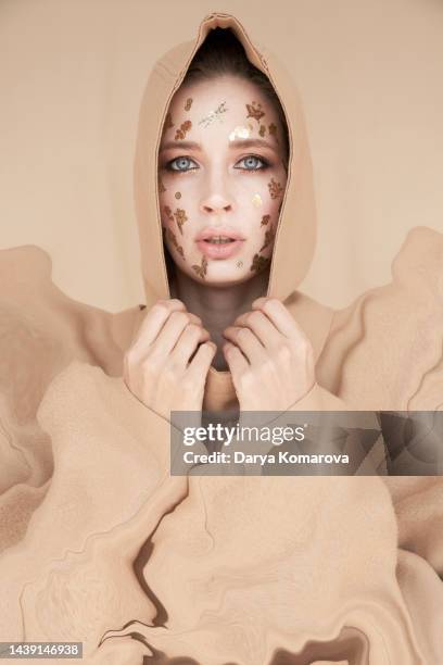a young woman in a hood and beige suit stands on a beige background with gold decorative stickers on the face. the concept of islam woman, halloween party, beauty, makeup, surreal life. - girl power stickers stock pictures, royalty-free photos & images
