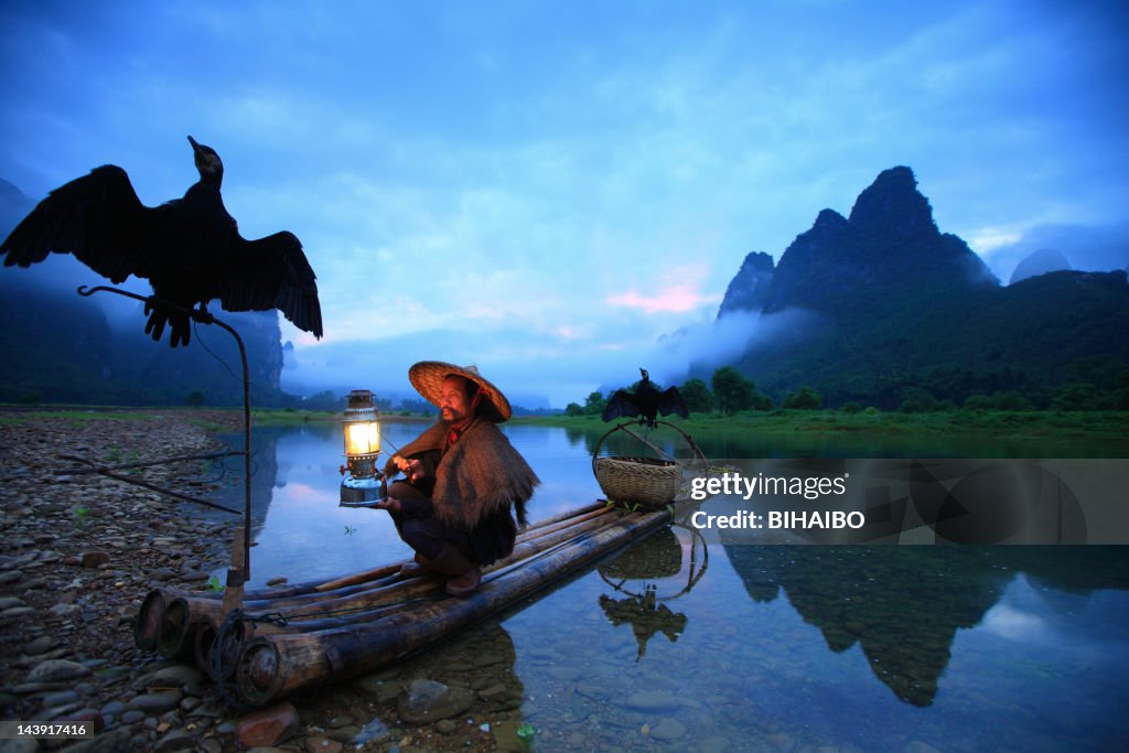 Fisherman holding flashlight and two crows