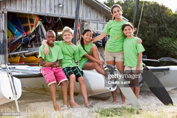 teenager and children in front of water sports equipment shack - camp counselor stock pictures, royalty-free photos & images