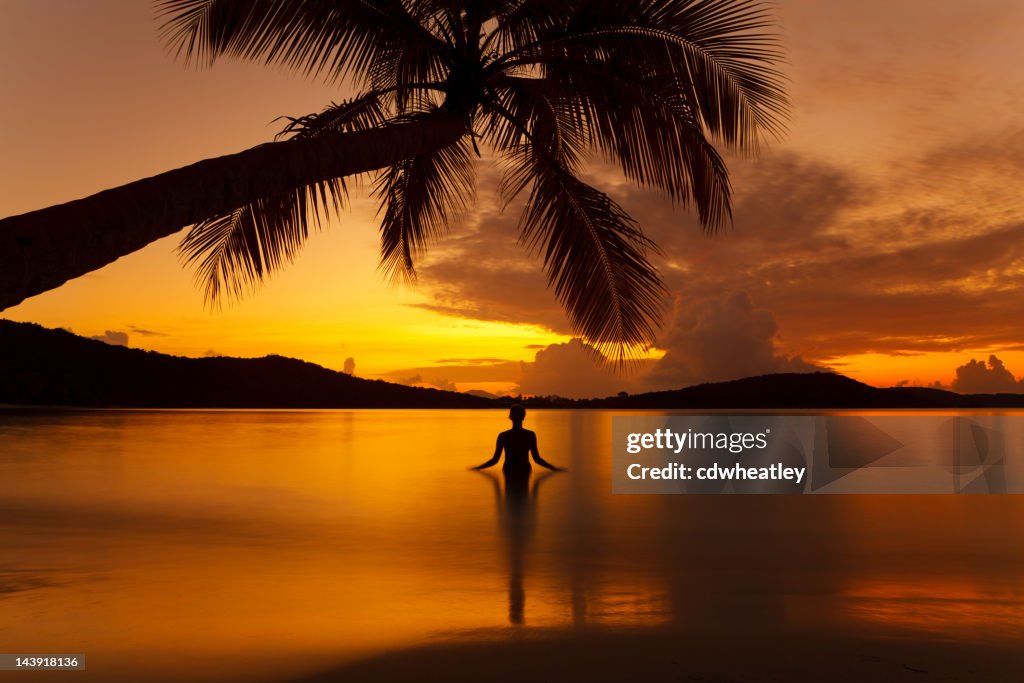 Silhouette woman meditating in water during sunset at a beach