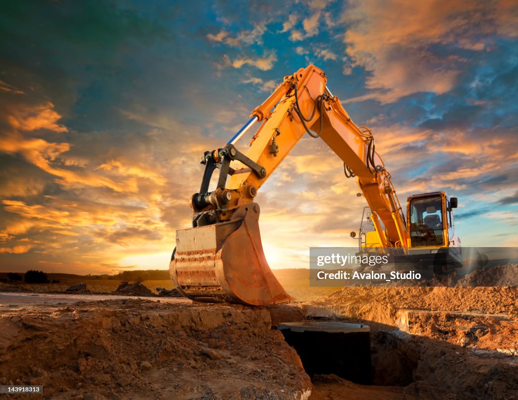 Excavator at a construction site against the setting sun.