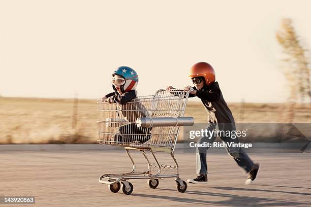 niños en cascos raza una cesta de compras - carro de corrida fotografías e imágenes de stock