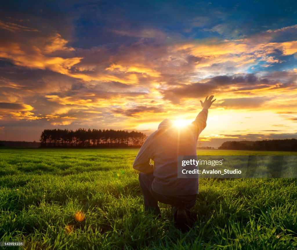 Man on meadow praying to god facing the sun