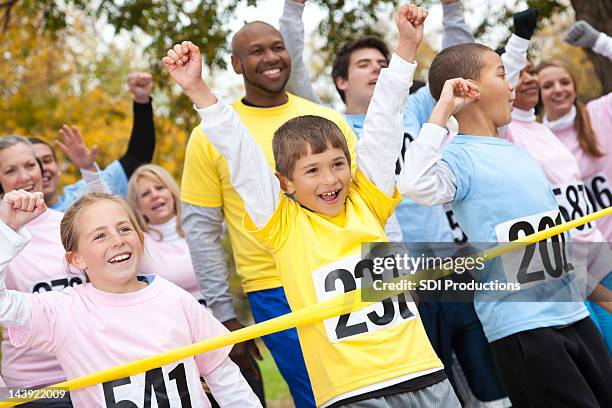 excited children and adults happily crossing a race finish line - sweet charity stock pictures, royalty-free photos & images