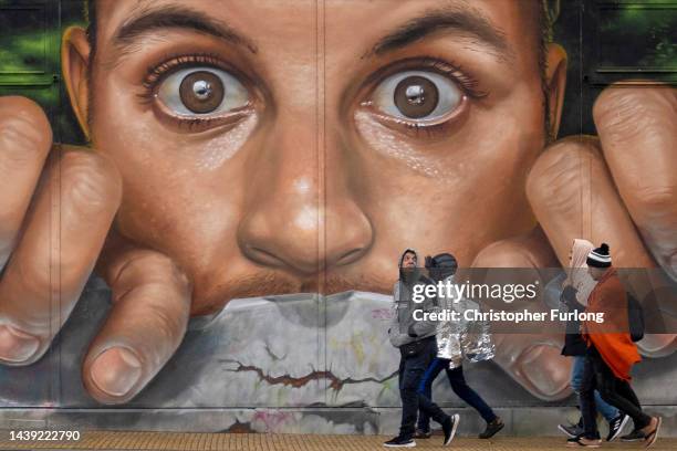 Group of migrants in central Calais walk past a mural by artist Braga Last One on November 05, 2022 in Calais, France. Around 2,000 migrants are...