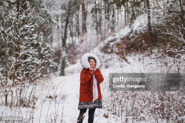 rothaarige frau in roter jacke mit fell und hut im winterwald. hübsche frau, die urlaub genießt. mädchen in kapuze in der natur. fühle glück. raureif und schnee auf bäumen. urlaub in den bergen - februar stock-fotos und bilder