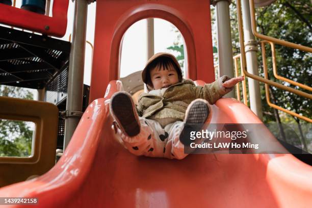 a cute baby girl is happily playing with the slide - bébé jeu photos et images de collection
