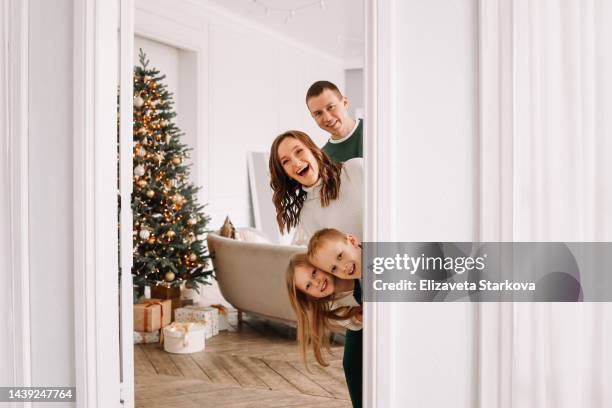 the concept of christmas shooting. portrait of funny and smiling faces of people looking out of the door and looking into the camera. a happy family with two teenage children spending time together during the christmas holidays in a decorated scandinavian - happy holidays family stock pictures, royalty-free photos & images