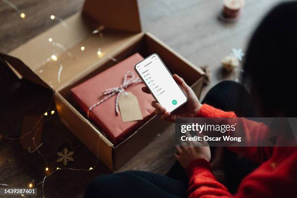 young woman checking christmas shopping list on smart phone - christmas gift boxes stock pictures, royalty-free photos & images