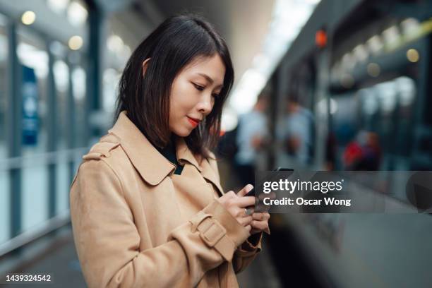 young asian businesswoman working with smartphone while waiting for train on the platform at railway station - waiting for train stock pictures, royalty-free photos & images