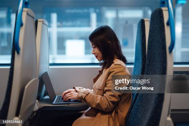young asian businesswoman working on laptop while commuting by train - railways uk stock-fotos und bilder
