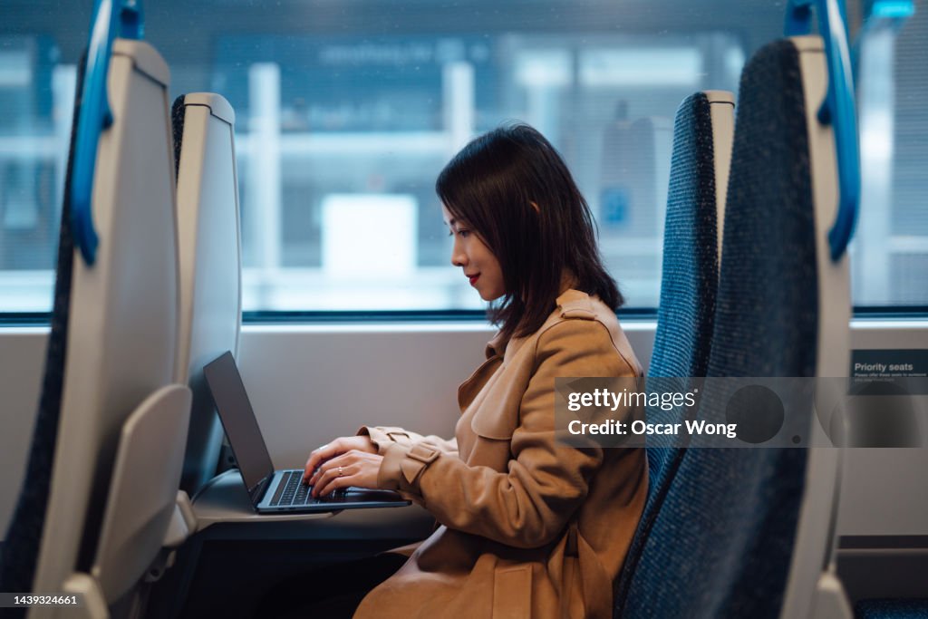 Young Asian businesswoman working on laptop while commuting by train