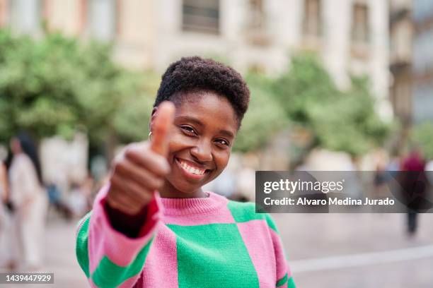front view of a young african american woman making the thumbs up gesture with her hand while looking at the camera. - duim stockfoto's en -beelden