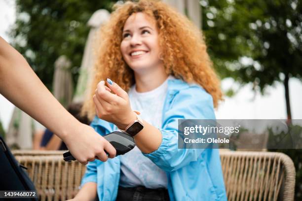 girl using her smartwatch to make a payment at the outdoor cafe - smartwatch pay stock pictures, royalty-free photos & images