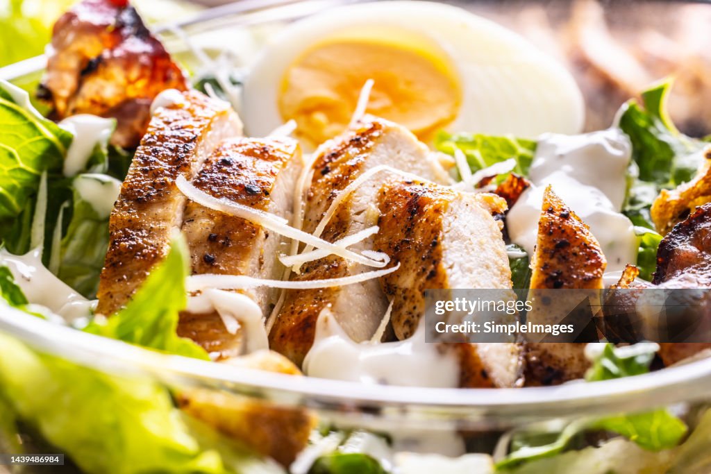 Delicious Caesar salad with grilled chicken slices in a glass bowl.
