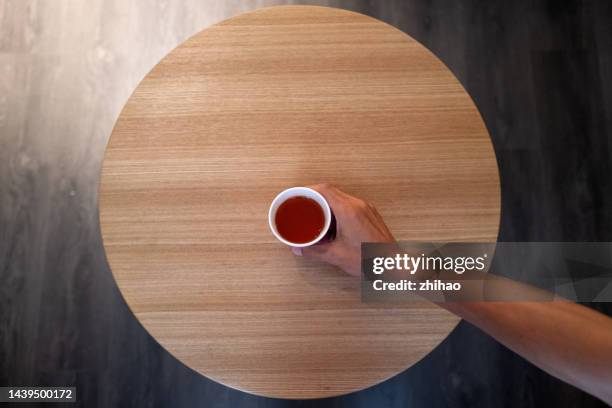 human hand holding tea cup on round table - graphischer druck stock-fotos und bilder