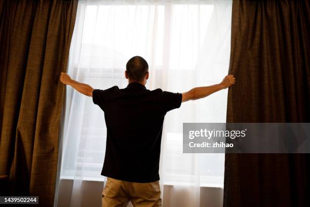 back view of asian man opening curtain - chiudere foto e immagini stock