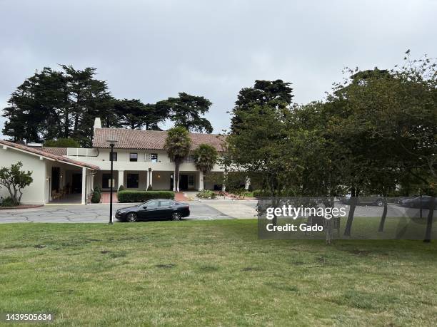 Wide shot of the Presidio Officer's Club, on an overcast day, with a black parked car, trees, and a bench at mid-ground and grass in the foreground,...