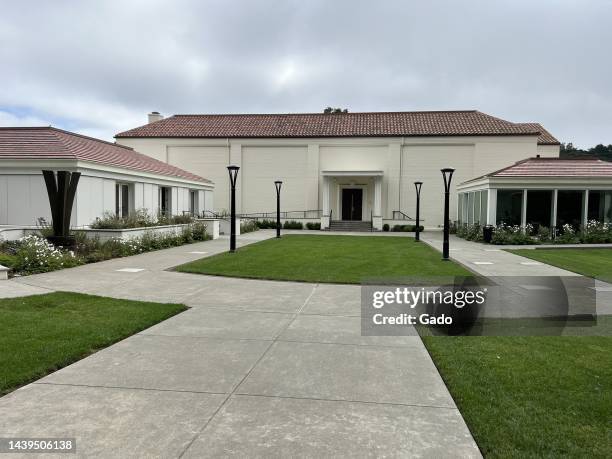 Wide shot of a concrete path and manicured lawns leading to the white-walled and red-roofed Presidio Theatre buildings on an overcast day in the...