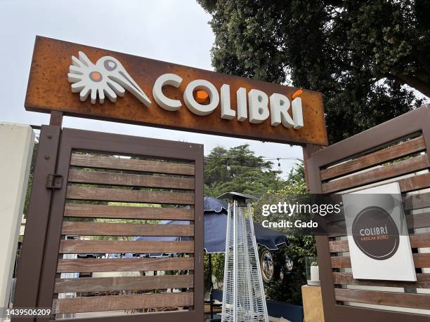 Low-angle view of the Colibri Mexican Bistro entrance, with one slatted metal and wood door open to reveal outdoor heaters and umbrellas in a...