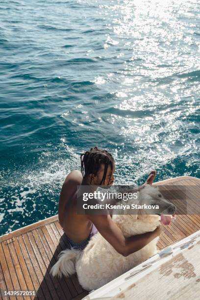 black young man in shorts rides a yacht on the sea with a white dog golden retriever - anti racisme stockfoto's en -beelden