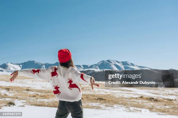 happy young woman with raised hands on the background of blue sky and winter mountains in winter looking at the landscape. christmas travel concept - women's winter clothes stockfoto's en -beelden