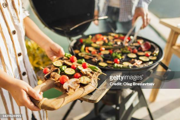 woman's hands holding fresh vegetables on skewers for outdoor barbecue - grillen stock-fotos und bilder