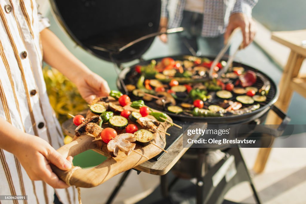 Woman's hands holding fresh vegetables on skewers for outdoor barbecue