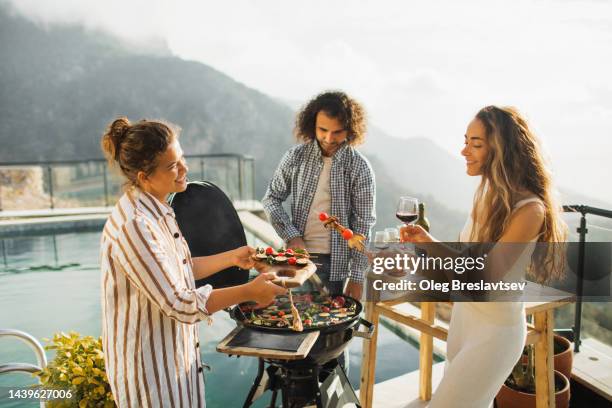 friends cooking on grill and drinking wine outdoors on poolside with mountain view - poolside glamour stock pictures, royalty-free photos & images