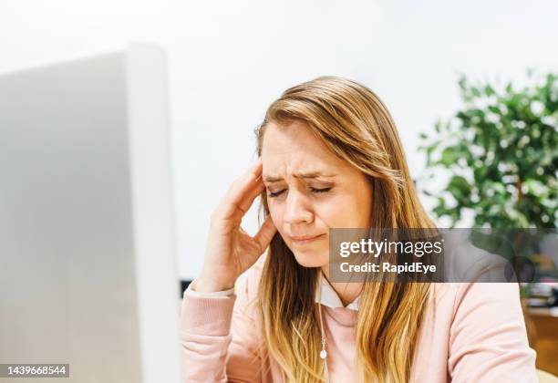 schöne frau mit langen blonden haaren sieht unglücklich aus, als sie an ihrem computer in einem büro sitzt, trauernd oder mit kopfschmerzen - woman silver hair young stock-fotos und bilder