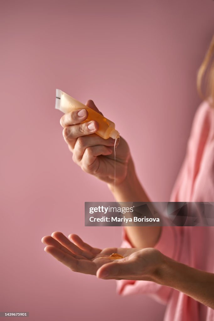 A girl in pink pours a gel-texture cosmetic onto her hand.