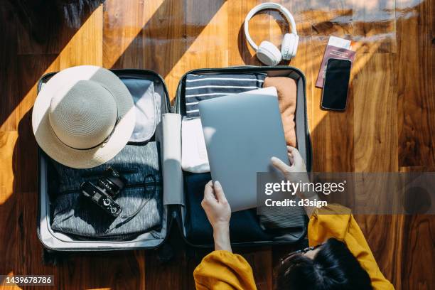 overhead view of young asian woman sitting on the floor in her bedroom, packing a suitcase for a trip. getting ready for a vacation. traveller's accessories. travel and vacation concept. business travel - 新常態 概念 個照片及圖片檔