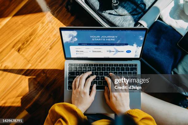 high angle shot of young asian woman booking flight tickets on airline website online with laptop, with packed suitcase by her side. travel planning. booking a holiday online. travel and vacations concept. ready to travel. business trip planning - phone screen at airport stockfoto's en -beelden