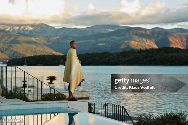 man wrapped in blanket standing by swimming pool - exclusive travel stock pictures, royalty-free photos & images