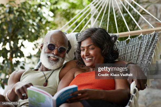 happy couple reading book while lying in hammock - hammock stock pictures, royalty-free photos & images