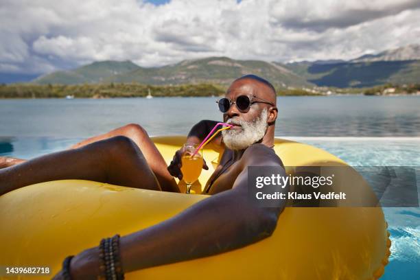man drinking juice in inflatable ring - pool relaxation stock pictures, royalty-free photos & images